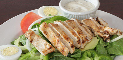 sliced grilled chicken on salad with dressing on side